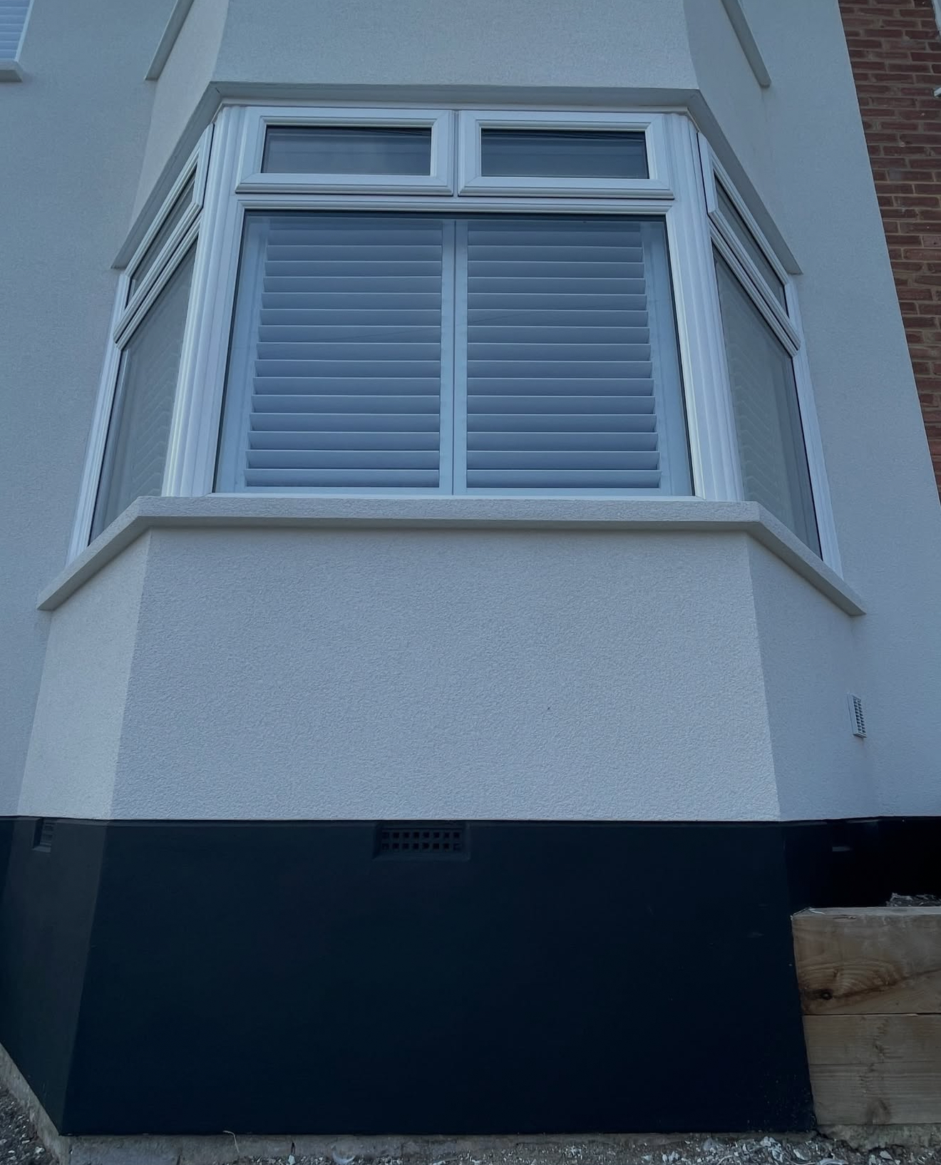 Rendered bay window with a dark plinth